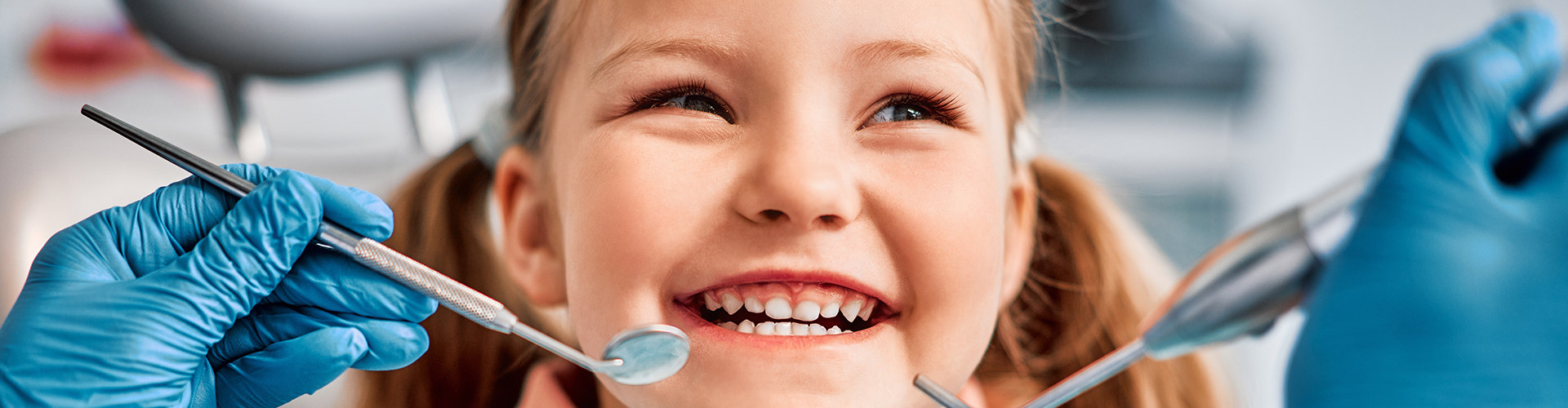 gloved hands holding dental tools by girl's mouth
